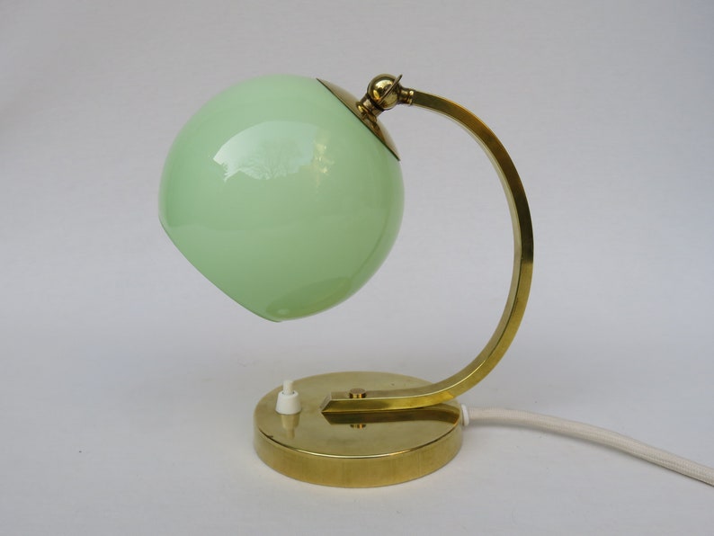 Peut inclure: Une lampe de bureau en laiton avec un abat-jour en verre vert. La lampe a un bras incurv&eacute; et une base ronde.