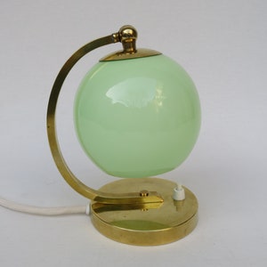 Peut inclure: Une lampe de table en laiton avec un abat-jour en verre vert. La lampe a un design simple avec un bras incurv&eacute; et une base ronde.