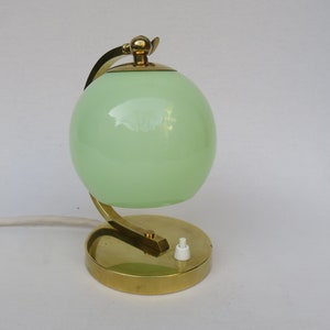 Peut inclure: Une lampe de table en laiton avec un abat-jour en verre vert en forme de globe. La lampe a un bras incurv&eacute; et une base ronde.
