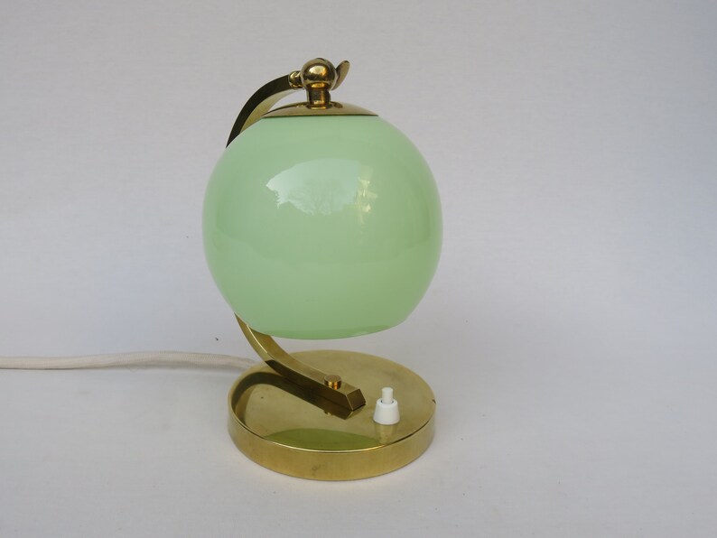Peut inclure: Une lampe de table en laiton avec un abat-jour en verre vert en forme de globe. La lampe a un bras incurv&eacute; et une base ronde.
