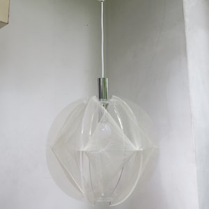 Könnte beinhalten: Eine weiße, runde, geometrische Pendelleuchte mit Chrom-Finish. Die Leuchte besteht aus dünnem, weißem, schnurartigem Material, das ein netzartiges Muster erzeugt.