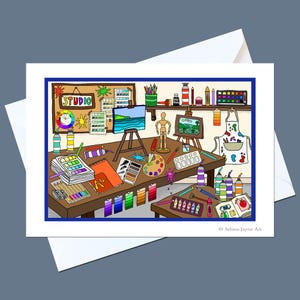 以下が含まれることがあります： アーティストのアトリエを描いたカラフルな漫画風イラストのグリーティングカード。木製のデスクには絵の具のチューブ、筆、パレット、スケッチブック、デッサン人形、イーゼルに立てかけられたキャンバスが描かれています。STUDIOという文字が見えます。