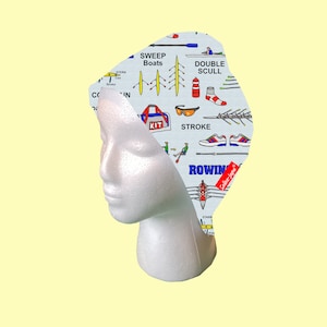 May include: A white and blue patterned fabric headband with illustrations of rowing equipment, including oars, a boat, and a person rowing. The text "ROWING" is printed in blue letters on the headband. The text "Solina-Jame" is printed in red letters on the headband.
