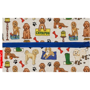 May include: A beige zippered pouch with a blue zipper. The pouch is covered in a repeating pattern of brown and white cavapoo dogs, paw prints, bones, and other dog-related items. The text "CAVAPOO" is printed on a sign held by one of the dogs.