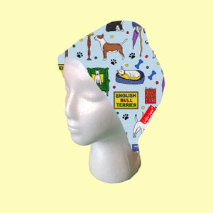 May include: A blue and white patterned surgical cap with a design of English bull terriers, dog treats, and bones. The cap has the text "English Bull Terrier" and "Dog Treats 9-18" printed on it.
