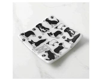 May include: A white, diamond-shaped decorative dish with a black dog and paw print pattern. The dish features various dog breeds in silhouette, along with paw prints and a stylized barn. The design is repeated across the surface.