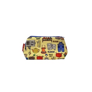 May include: A yellow zippered pouch with a blue zipper and a red tag. The pouch is covered in colorful illustrations of pottery tools and phrases like "Glazed One Day" and "Bisque".