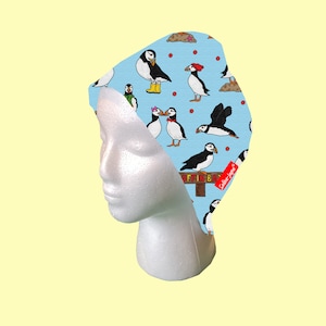May include: A blue and white patterned fabric headband with a design of puffins and the text "Puffin Bar". The headband is on a white mannequin head.