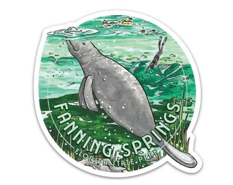 May include: A round sticker with a green, blue, and white background. The sticker features a cartoon manatee swimming in the water. The text "Fanning Springs Florida State Park" is written around the manatee.