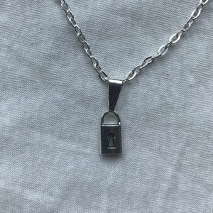 May include: A silver chain necklace with a small padlock pendant. The padlock has a keyhole cutout.