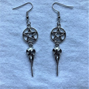 Puede incluir: Pendientes de plata con un dije de pentagrama y un colgante de cráneo de pájaro.