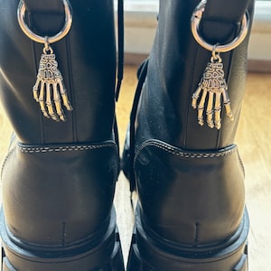 Puede incluir: Botas de cuero negro con suelas de plataforma gruesas y abalorios de mano de esqueleto plateados unidos a la parte posterior de cada bota.