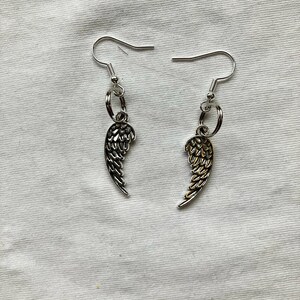 May include: A pair of silver earrings with a dangling angel wing charm. One wing is silver and the other is gold.