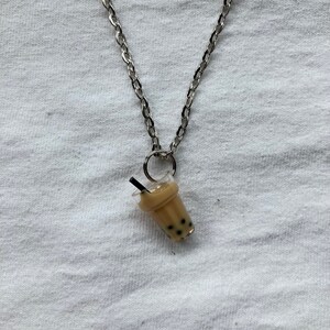 Könnte beinhalten: Eine silberne Kettenkette mit einem Anhänger in Form eines braunen Bubble Teas mit schwarzen Tapiokaperlen und einem schwarzen Strohhalm.