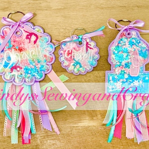 May include: Three colorful keychains with a floral design, each with a different shape. The keychains have a ribbon and tassel design. One keychain has a ballet slipper design. The keychains have the name "Charli" on them.