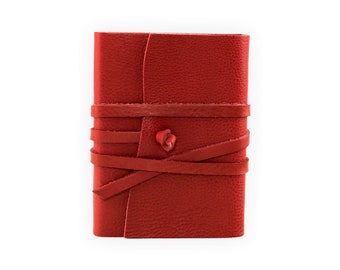 May include: A red leather journal with a leather strap closure. The journal is tied with a leather cord and has a decorative knot.
