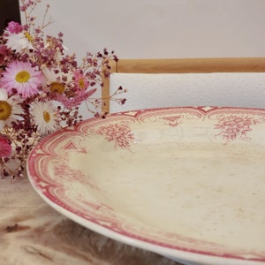 Puede incluir: Un plato de servir grande de cerámica blanca con un diseño floral rosa y blanco. El plato tiene un borde festoneado y es perfecto para servir una variedad de platos.