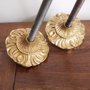Op de afbeelding: Twee gouden metalen decoratieve eindstukken met een gedetailleerd bloemmotief. Elk eindstuk heeft een schroefdraadstang die vanuit het midden uitsteekt.