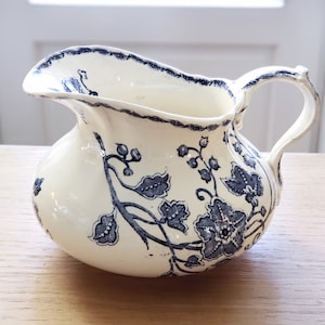 Peut inclure: Un pot à crème en céramique blanche avec un motif floral bleu. Le pot à crème a un corps arrondi et une poignée incurvée.