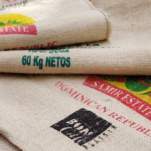 Puede incluir: Primer plano de una pila de sacos de arpillera con texto verde y rojo. El saco superior tiene el texto "STATE" y "60 Kg NETOS". El saco inferior tiene el texto "DOMINICAN REPUBLIC" y "SAMIRESTHE".