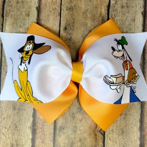 May include: A handmade hair bow in white and yellow. The bow features cartoon images of a dog on a white center. The bow is layered over a bright yellow ribbon.