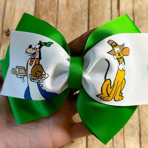 May include: Green and white bow with a cartoon image of Goofy holding a plate of food and Pluto sitting on the other side.
