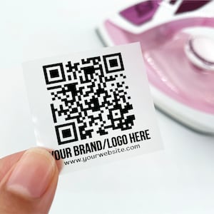 Peut inclure: Un autocollant rectangulaire transparent avec un code QR noir et le texte "YOUR BRAND/LOGO HERE www.yourwebsite.com".