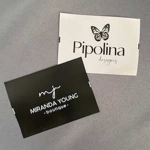 Può includere: Due biglietti da visita, uno nero con testo bianco e l'altro bianco con testo nero. Il biglietto nero ha il testo "mj MIRANDA YOUNG .boutique." Il biglietto bianco ha un logo a forma di farfalla e il testo "Pipolina designs".