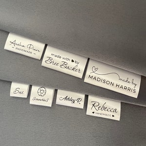Peut inclure: Étiquettes en satin blanc avec du texte noir, présentant des noms et des phrases comme "Aisha Piere - Fait main", "fait avec amour par Bree Backer", "fait par MADISON HARRIS", "Sue Scrunchies", "Ashley R" et "Rebecca - Fait main".