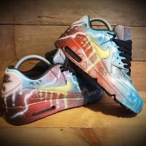 May include: A pair of custom-painted Nike Air Max 90 sneakers. One shoe features a blue, yellow, and red lightning bolt design, while the other shoe features a red, yellow, and blue lightning bolt design.