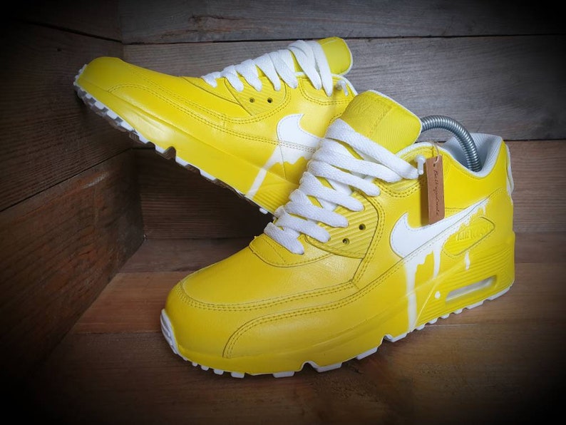 May include: A pair of yellow leather sneakers with white laces and a white swoosh logo. The sneakers have a white paint drip design on the side.