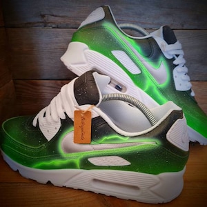 May include: Green and white custom-painted Nike Air Max 90 sneakers with a lightning bolt design. The shoes have a black swoosh and a white midsole.