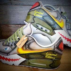 May include: A pair of custom-painted Nike Air Max 90 sneakers with a camouflage pattern, yellow and red accents, and the text "Limited Edition".