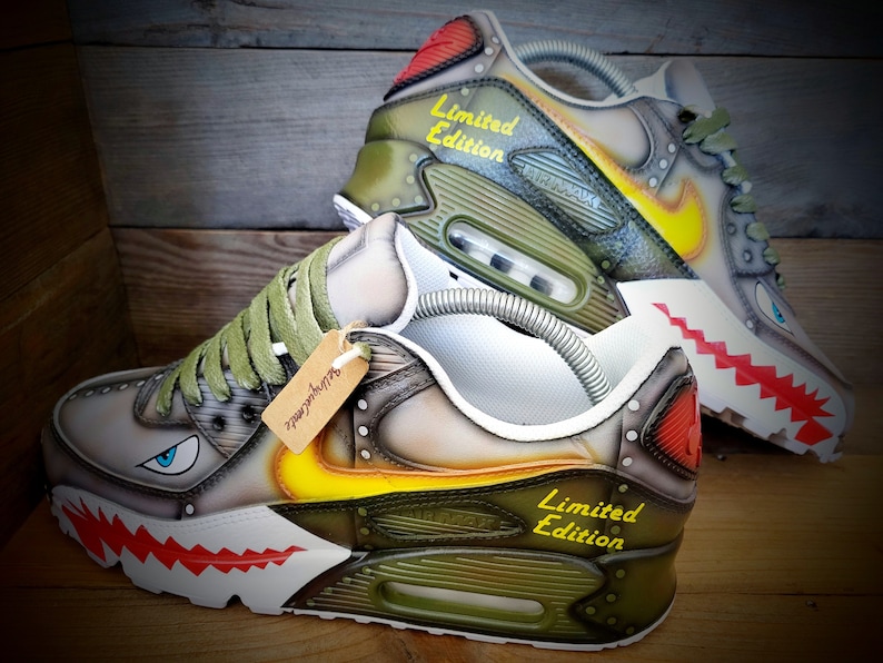 May include: A pair of custom-painted Nike Air Max 90 sneakers with a camouflage pattern, yellow and red accents, and the text "Limited Edition".