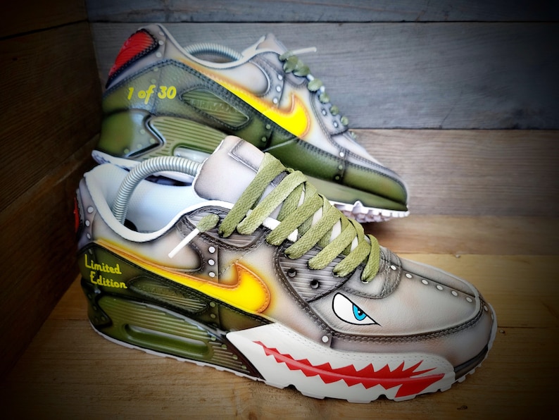 May include: A pair of custom-designed green and white sneakers with a shark tooth design on the sole. The sneakers have a yellow and orange flame design on the side and the text "Limited Edition" and "1 of 30" on the shoes.