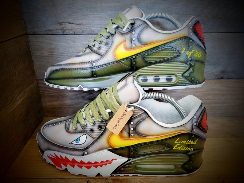 May include: Custom-painted Nike Air Max 90 sneakers with a camouflage and steampunk design. The shoes feature a yellow and green color scheme, a shark tooth design on the sole, and the text "Limited Edition" and "1 of 30" on the sides.