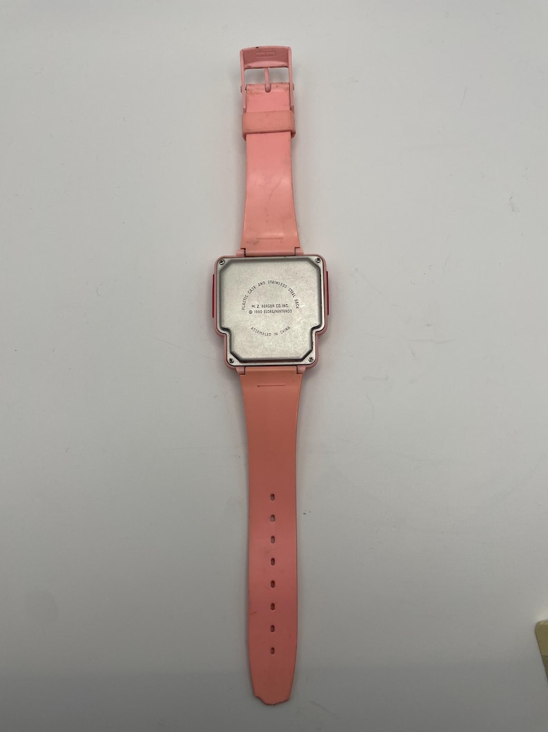 Puede incluir: Un reloj digital rosa vintage con una esfera rectangular y una correa a juego. El reloj tiene una caja de pl&aacute;stico y una parte trasera de acero inoxidable. La correa tiene m&uacute;ltiples orificios de ajuste. El reloj est&aacute; ensamblado en China.