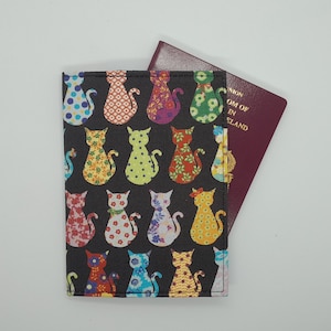 May include: A black passport holder featuring a repeating pattern of patterned cat shapes. The cats are decorated with floral and polka dot designs. A burgundy passport is partially visible inside the holder.