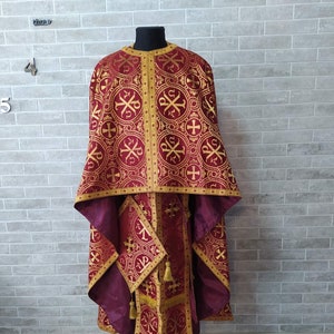 May include: A burgundy liturgical vestment with gold embroidery. The vestment features a cross pattern and intricate details.