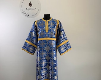 Könnte beinhalten: Ein blaues und goldenes liturgisches Gewand mit geometrischem Muster. Das Gewand befindet sich auf einem Mannequin und hat einen hohen Kragen und lange Ärmel.