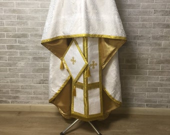 May include: White liturgical vestment with gold trim and embroidery. The vestment is displayed on a stand.