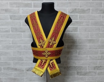 Könnte beinhalten: Ein rotes und goldenes Stoffband mit einem Kreuzmuster. Das Band wird auf einem Mannequin auf einem Stativ vor einer Backsteinwand ausgestellt.