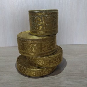 May include: Four spools of gold ribbon with a cross and floral pattern. The ribbon is stacked on top of each other.