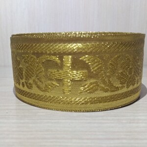 May include: Gold trim with a cross and floral design. The trim is woven and has a subtle shimmer.