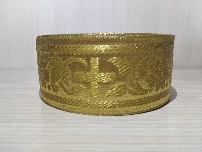 May include: Gold trim with a cross and floral design. The trim is woven and has a subtle shimmer.