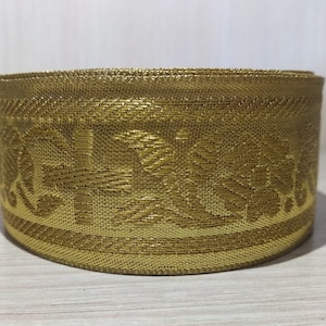 May include: Gold trim with a floral pattern. The trim is rolled up into a circle.