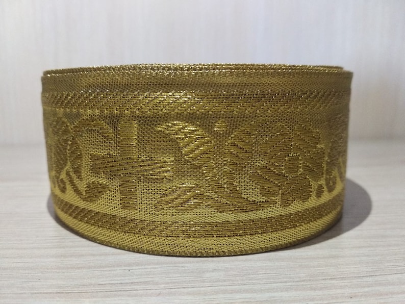 May include: Gold trim with a floral pattern. The trim is rolled up into a circle.