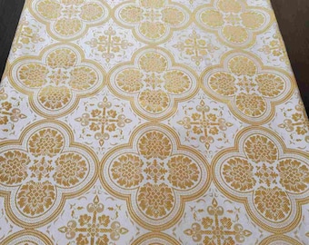 Pode incluir: Tecido branco com um padrão repetido de quadrifólios dourados. Os quadrifólios têm um desenho floral detalhado.