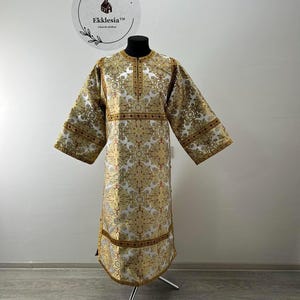 May include: A gold and white brocade liturgical vestment with a cross design and red trim. The vestment is displayed on a mannequin.