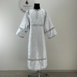 May include: White liturgical vestment with silver trim and a silver embroidered design. The vestment is displayed on a mannequin.